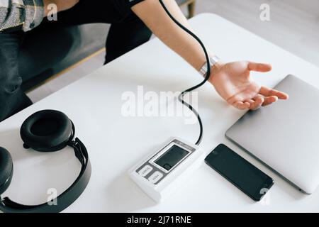 Junger Mann, der seinen Blutdruck auf dem Sofa im Wohnzimmer misst. Mit modernen Tonometer, erleben Hypertonie durch Stress verursacht. Stockfoto