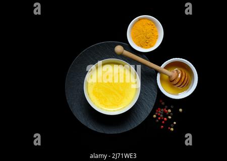 Kurkuma-Milch in Schale, Kurkumapulver und Honig mit Honigloeffel, Goldene Milch Stockfoto