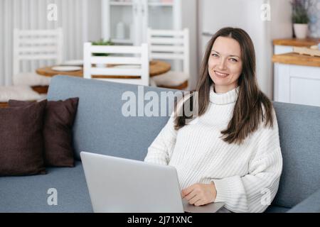 Junge Frau mit Laptop sitzt auf der Couch. Stockfoto