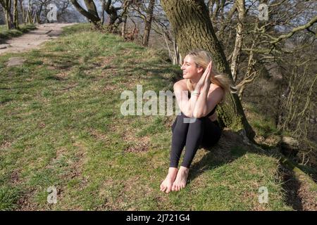 Schöne Frau, die unter Bäumen im Freien Yoga praktiziert Stockfoto