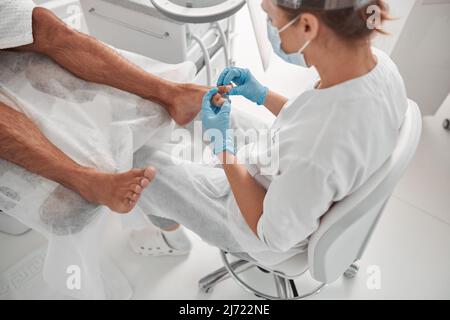 Meister in blauen Handschuhen überprüft Nägel des Mannes vor dem Eingriff im Schönheitssalon Stockfoto