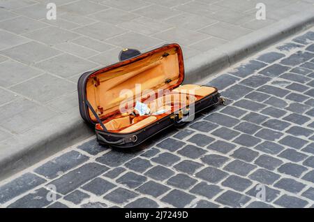 Das offene Geigengehäuse liegt auf altem Kopfsteinpflaster in der Stadt. Straßenmusiker sammelt Geld Stockfoto