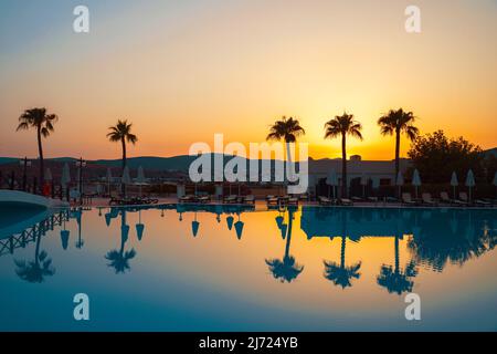 Palmen spiegeln sich in türkisfarbenem Wasser an einer tropischen Küste während des Sonnenuntergangs. Stockfoto
