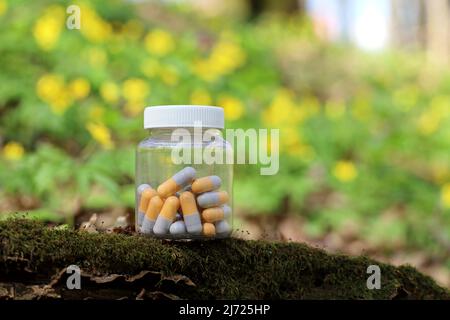 Pillen auf grünem Naturhintergrund, Flasche mit Kapseln im Frühlingswald. Konzept der natürlichen Vitamine und Apotheke, Kräutermedizin Stockfoto