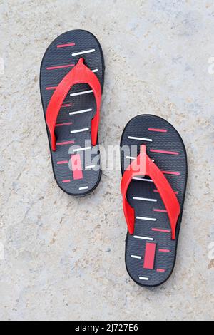 Nahaufnahme des roten schwarzen Slippers auf unscharfem graubraunen Hintergrund. Stockfoto