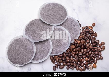 Draufsicht auf Kaffeepads und Kaffeebohnen auf einer Marmoroberfläche als Beispiel für verschiedene Kaffeerohprodukte. Flache Lay-Komposition Stockfoto