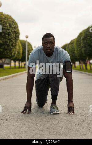 Sportler bereit zum Laufen. Porträt eines jungen, athletischen afroamerikanischen Mannes in Startposition im Park und beim Betrachen der Kamera Stockfoto