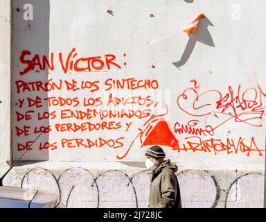 Mann in Gesichtsmaske an der Wandwand in Lavapiez, Madrid vorbei Text-Graffiti: San Victor; Mäzen der Künstler Muros Tabacalera 2019 Stockfoto