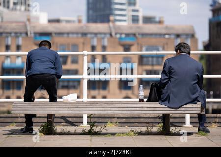 Zwei Männer besetzen eine Bank am Flussufer, einer steht auf, um am 5.. Mai 2022 in London, England, Butler's Wharf an der Southbank zu verlassen. Stockfoto