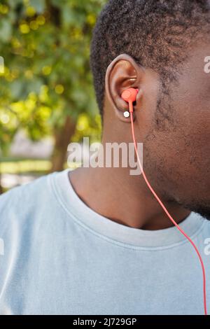 Unkenntlich Schwarzer Kerl, der Musik durch moderne rote Ohrstöpsel im Freien hört Stockfoto