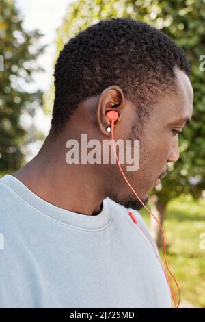 Profilportrait eines jungen afroamerikanischen Mannes, der Ohrring trägt und Musik über Kopfhörer im Freien hört Stockfoto