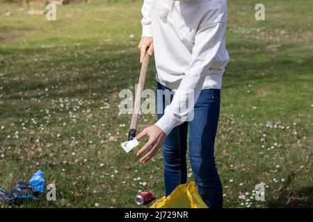 Nicht erkennbarer junger Mann, der mit einem Werkzeug Plastik aus dem Boden in einer Freiwilligensammlung sammelt Stockfoto