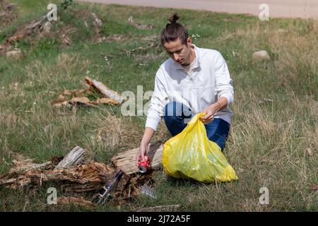 Junger Mann mit Bun-Frisur hockt sich zum Abfall und holt ihn in einem gelben Müllbeutel Stockfoto