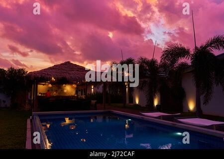 Ein sanfter Sonnenuntergang Himmel über einem reetgedeckten Bungalow. Ein exotisches Resort in den Tropen. Stockfoto