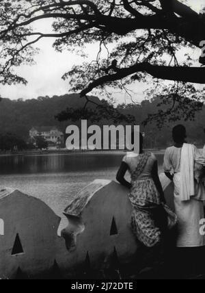 Die Königliche Tour: Ceylon - Kandy Lake -- H.M. die Königin und H.R.H. der Herzog von Edinburgh werden Kandy vom 18.. Bis 20.. April 1954 besuchen. Die Stadt Kandy liegt in einem Tal zwischen Hügeln, und ist selbst auf einer Höhe von etwa 1500 ft. Dieser künstliche See liegt direkt neben der Stadt. Einige einheimische Frauen halten an der Balustrade inne und blicken über das Wasser zum „Tempel des Zahns“. Ein Blick auf den Kandy Lake, mit Blick auf den 'Tempel des Zahns'. 12. April 1954. (Foto von Rosemary Gilliat, Camera Press). Stockfoto