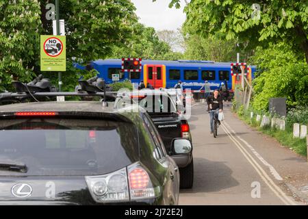 Stationäre Autos stehen Schlange und stehen im Leerlauf, während ein Zug der South Western Railway die Signalbox Vine Road von Network Rail in Barnes, London, SW13, England, Großbritannien, passiert