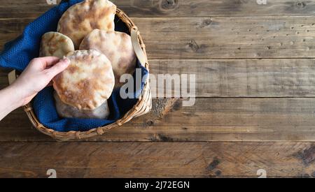 Die Hände der Frau legen hausgemachtes Pita-Brot in einen Holzkorb auf einen alten Holztisch. Speicherplatz kopieren. Stockfoto