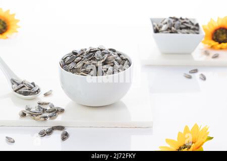 Zwei Schalen Sonnenblumenkerne mit Sonnenblumen auf weißem Hintergrund. Selektiver Fokus. Stockfoto