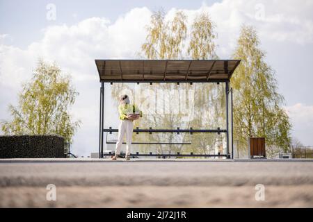 Frau mit Blumentopf an der modernen Bushaltestelle Stockfoto