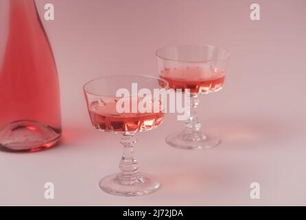 Zwei Kristallgläser und eine Flasche Rosé-Sekt oder Champagner auf pastellrosa Hintergrund. Urlaubskonzept. Minimale kreative Komposition mit Kopierplatz. Stockfoto