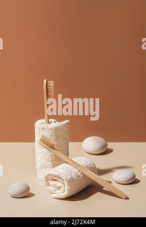 Zahnbürsten aus Bio-Bambus aus Holz, Handtücher und weiße Meeressteinchen auf Terrakotta- und beigefarbenem Hintergrund. Natürliche Schönheit und Gesundheit Konzept. Umweltfreundliches Design ohne Verschwendung mit Platz für Kopien. Stockfoto