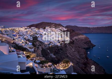 Panoramablick auf den Sonnenuntergang über dem beleuchteten Dorf Oia Stockfoto