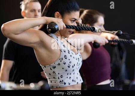 Seitenansicht einer entschlossenen jungen Frau, die im Fitnessstudio mit einer Seilrolle geradeaus blickt Stockfoto