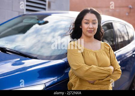 Porträt einer Frau, die mit gekreuzten Armen mit Blick auf die Kamera mit dem Auto steht Stockfoto