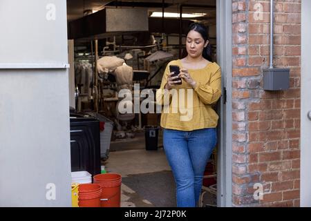 Junge Frau, die in Reinigungsmitteln arbeitet, Pause im Hinterzimmer und mit dem Handy. Stockfoto