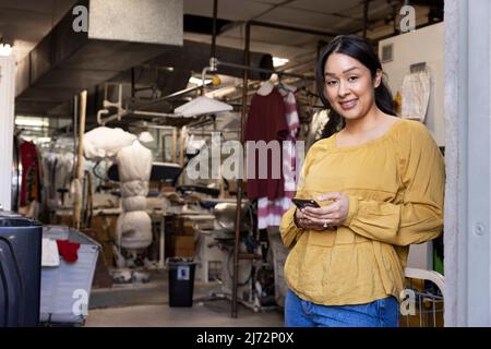 Porträt einer Frau, die ihr Telefon hinten benutzt, während sie bei der Reinigung arbeitet. Stockfoto