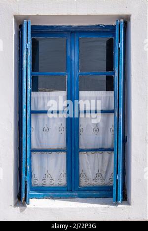 Fenster mit pastellblauen, offenen Holzfenstern an der weißen Wand. Kykladen Inselhaus Vorderansicht, griechische traditionelle Architektur. Stockfoto