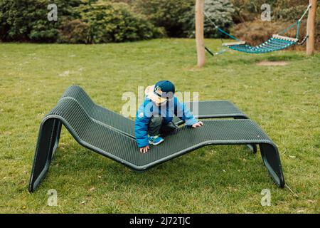 Ein kleiner Junge mit Sonnenbrille kriecht auf einer Parkbank Stockfoto