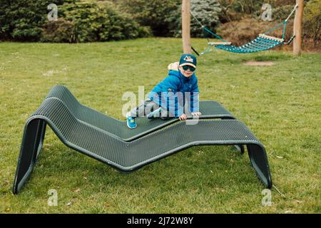 Ein kleiner Junge mit Sonnenbrille kriecht auf einer Parkbank Stockfoto