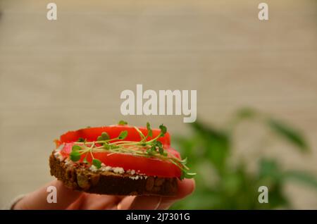 Das Mädchen kocht und isst zum Frühstück Salat, Tomate, Weichkäse. Veganes Sandwich mit Roggenbrot, Spinat, mikrogrün isoliert auf weiß, zu Stockfoto