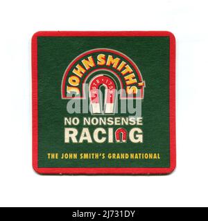 Eine Vintage-Biermatte, die als Werbeartikel für John Smith’s Bitter hergestellt wurde und für das Sponsoring des Grand National Steeplechase-Pferderennens 2005 wirbt, mit dem Firmenlogo und den Slogans „No Nonsense Racing“ und „The John Smith’s Grand National“. Stockfoto