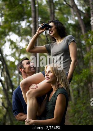 Frau, die auf den Schultern von Freunden sitzt und durch ein Fernglas im australischen Busch schaut Stockfoto