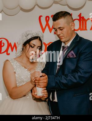 Bräutigam und Brauttuch halten in ihren Händen eine brennende Kerze, die den Herd der Familie symbolisiert. Slawische ukrainische russische Hochzeit Stockfoto