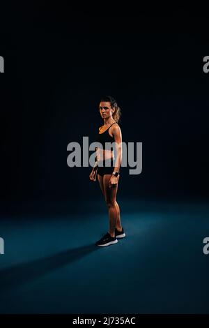 Porträt einer jungen Frau in Sportkleidung, die sich während des Trainings auf schwarzem Hintergrund entspannt Stockfoto