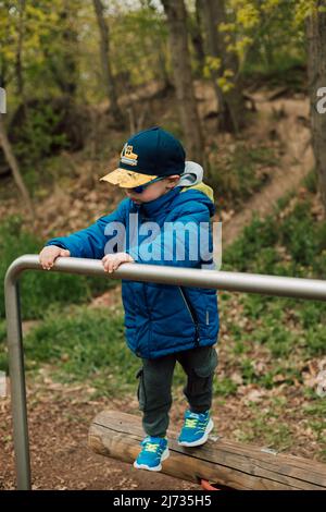 Ein Junge mit Jacke und Sonnenbrille steht im Park und lehnt sich an die Querlatte Stockfoto