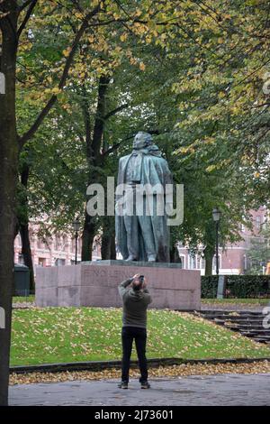 Mann, der die Statue des finnischen Dichters und Journalisten Eino Leino im Esplanade Park, Helsinki, Finnland, fotografiert. Stockfoto