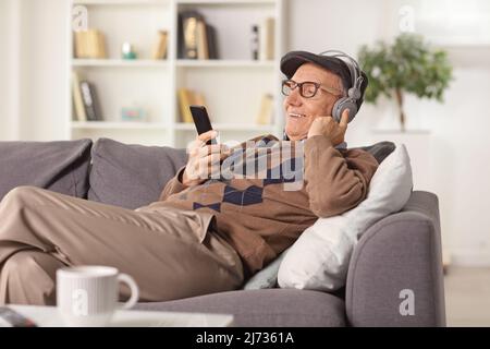 Rekaxed älterer Mann, der zu Hause auf einem Sofa sitzt und Musik von einem Smartphone hört Stockfoto