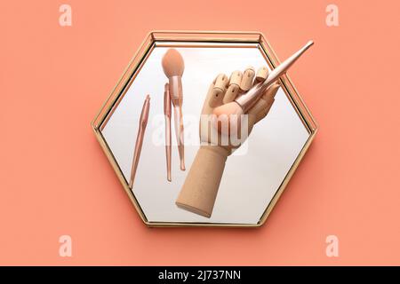 Holzhand mit Schminkpinsel und Spiegel auf rosa Hintergrund Stockfoto