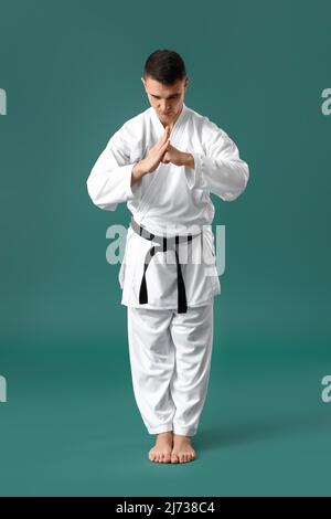 Mann, der rituelle Verbeugung vor dem Karate auf grünem Hintergrund ausführt Stockfoto