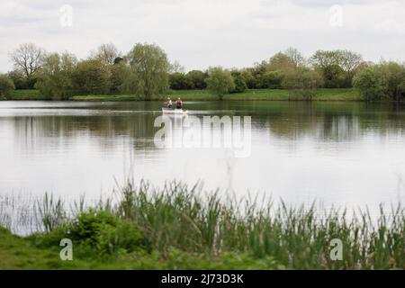 Zwei männliche Angler stehen auf und werfen eine Linie / gehen Angeln in einem kleinen Ruderboot in der Mitte eines Sees / Wasser, Großbritannien Stockfoto