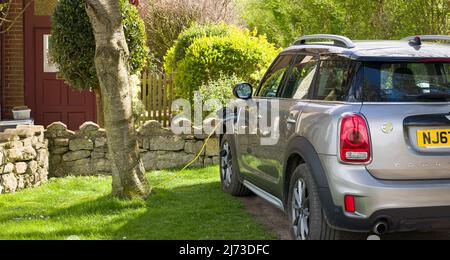 BUCKINGHAMSHIRE, Großbritannien - 09. April 2022. Elektroauto laden zu Hause. Elektrischer Mini Landmann parkte vor einem Haus, eingesteckt und aufgeladen. Stockfoto