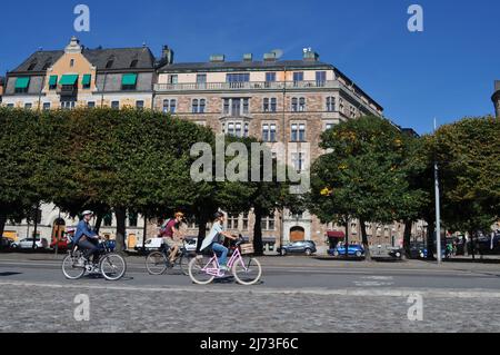 Drei Personen radeln im Sommer auf Radwegen am Strandvägen, am Ufer von Ostermalm, Stockholm, Schweden. Stockfoto