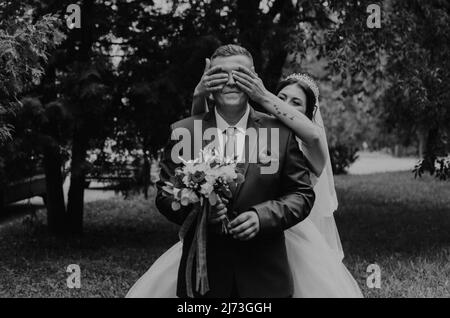 Europäische kaukasischen Mann Bräutigam in Anzug und Frau Braut im Hochzeitskleid Schleier Tiara auf dem Kopf. Erste Sitzung Brautpaar warten sieht Braut. Mädchen kommt Stockfoto