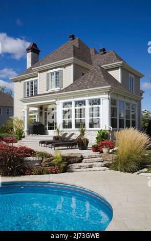 Gehobenes zweistöckiges Haus mit landschaftlich gestaltetem Hinterhof, Terrassenmöbeln und einem Pool im Erdgeschoss. Stockfoto