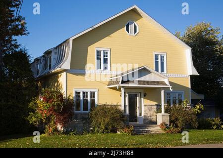 Gelbes zweistöckiges Haus mit Stein- und Holzplanken im Scheunenstil mit landschaftlich gestaltetem Vorgarten im Herbst. Stockfoto