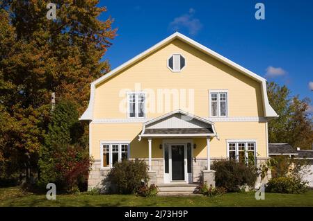 Gelbes zweistöckiges Haus mit Stein- und Holzplanken im Scheunenstil mit landschaftlich gestaltetem Vorgarten im Herbst. Stockfoto